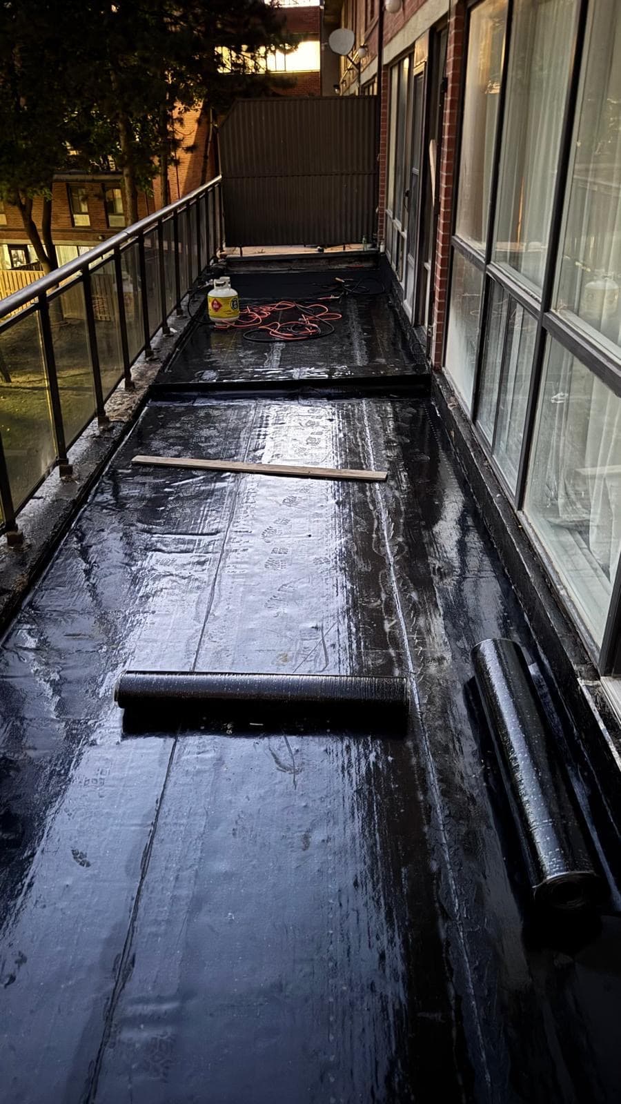 A long balcony deck newly covered with dark waterproofing membrane, with membrane rolls along it